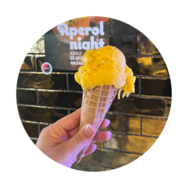 Eine Hand hält eine Eiswaffel mit Mangosorbet in die Höhe 