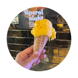 Eine Hand hält eine Eiswaffel mit Mangosorbet in die Höhe 